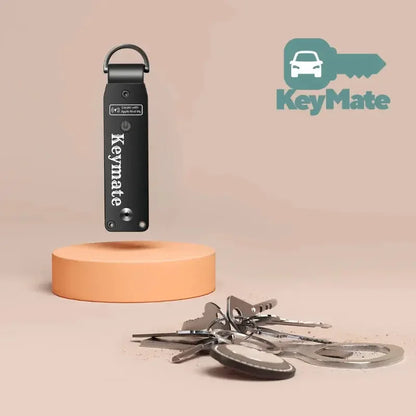 Fekete KeyMate kulcstartó, kulcsokkal és logóval, bézs háttéren